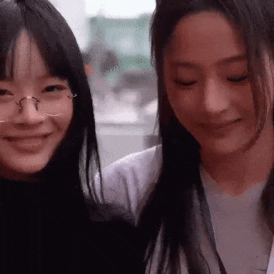 two young women are smiling and looking at the camera . one of the women is wearing glasses .