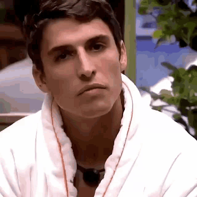 a man wearing a white robe and a black necklace looks at the camera