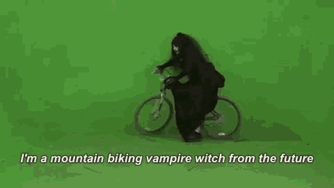 a vampire witch is riding a bike on a green screen while holding a sword .