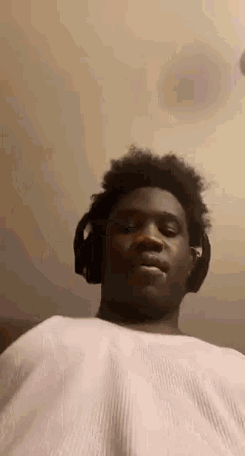 a young man wearing headphones and a white shirt is sitting on a bed .