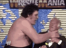 a shirtless wrestler is wrestling another wrestler in front of a wrestlemania sign