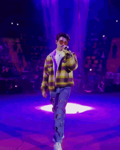 a man in a plaid jacket and ripped jeans is dancing on a stage .