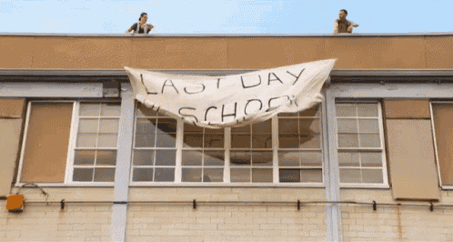 two people standing on top of a building with a banner that reads last day school