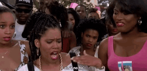 a group of women are standing in a crowd talking to each other . one of the women is wearing a pink tank top .