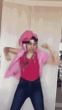a woman in a pink shirt and jeans is dancing in front of a white door .