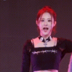 a woman with red hair is wearing a black crop top and a choker and smiling .