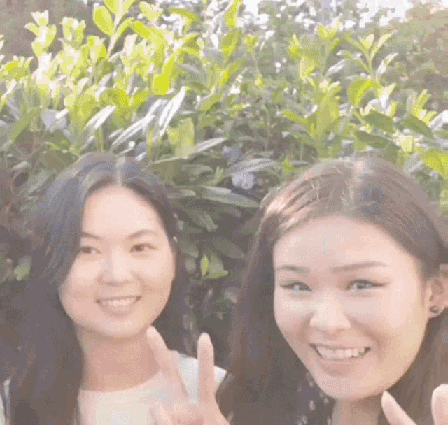 two women are standing next to each other in front of a bush .