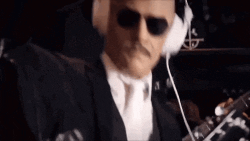 a man wearing sunglasses and headphones is playing a guitar .