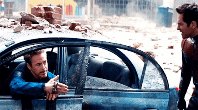 two men are standing next to each other in a car and talking .