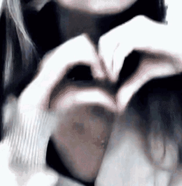 a close up of a woman making a heart shape with her hands