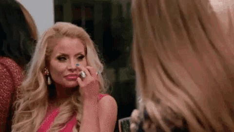 a woman is applying makeup to her face while looking at herself in the mirror .