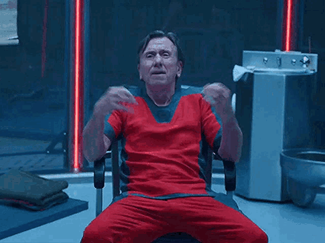 a man in a red shirt is sitting in a chair with the words namaste written above him .
