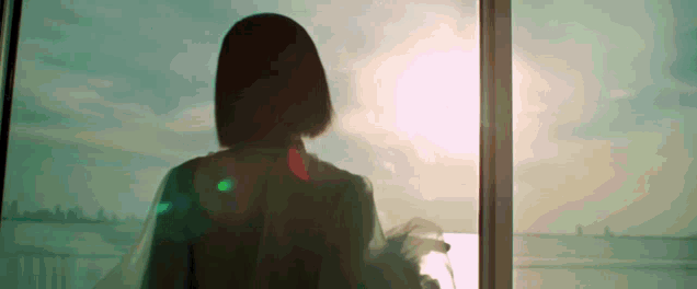 a woman is looking out of a window at sunset