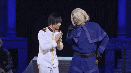 two men are standing next to each other on a stage and one of them is holding a rose .