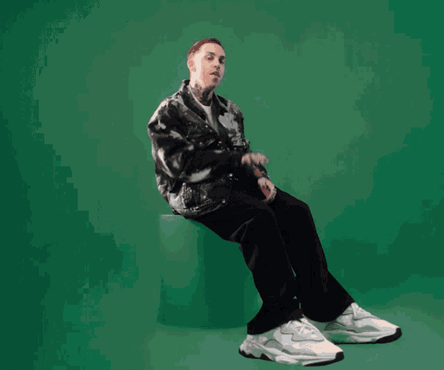 a man in a tie dye jacket sits on a green block