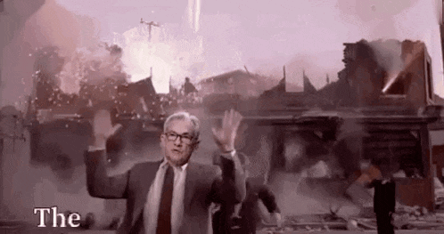a man in a suit and tie is standing in front of a destroyed building with his arms outstretched .