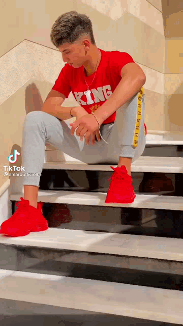 a young man wearing a red shirt that says king is sitting on a set of stairs