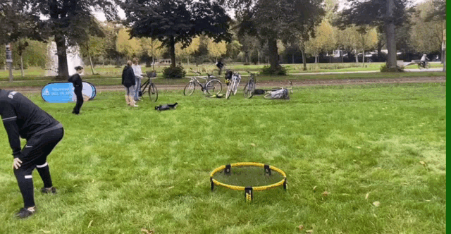 people playing a game in a park with a sign that says ' all are welcome ' on it