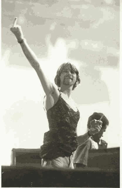 a man in a black lace tank top holds up his middle finger