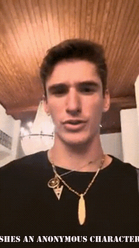 a man wearing a black shirt and a gold necklace with the words shes an anonymous character
