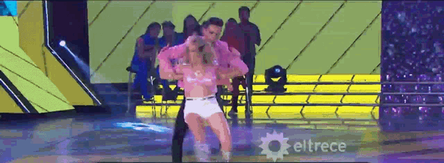 a woman in a pink top is dancing with a man on a stage with eltrece in the corner