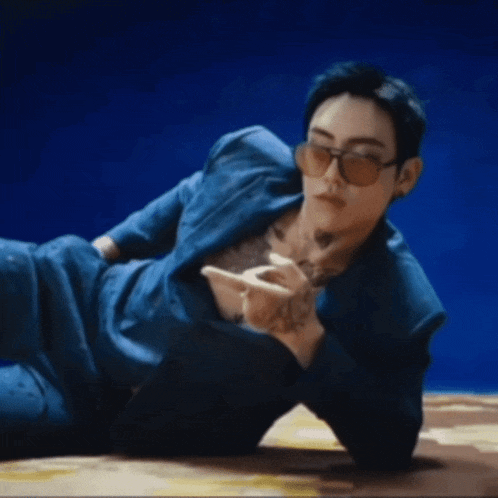 a man with a tattoo on his chest is laying on the floor wearing sunglasses and a blue suit