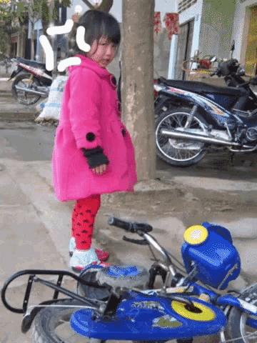 a little girl in a pink coat is standing next to a blue motorcycle that says ' yamaha ' on it