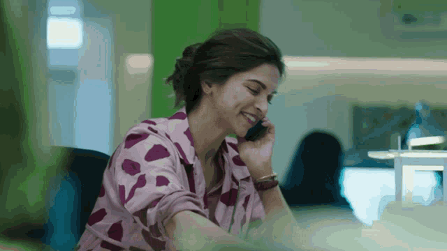 a woman in a pink polka dot shirt is smiling while talking on a cell phone