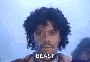 a man with curly hair and a beard is standing in front of a group of people and says `` beast '' .