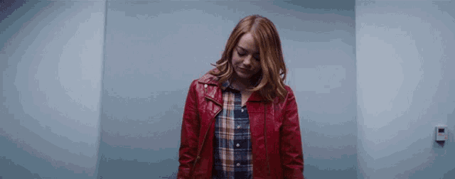 a woman in a red leather jacket and plaid shirt is standing in front of a blue wall