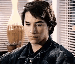 a man in a denim jacket is sitting in front of a window .