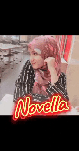 a woman wearing a hijab is sitting at a table with the name novella on the bottom right
