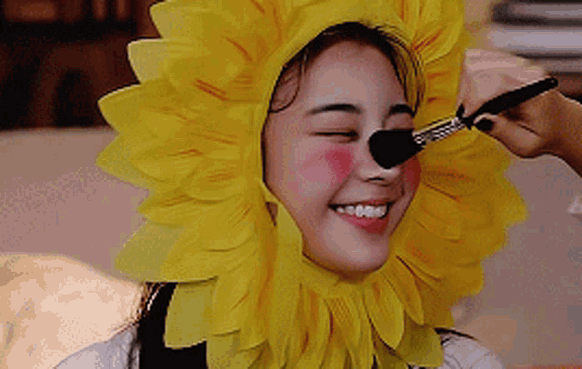 a woman wearing a sunflower hat is getting her makeup done .