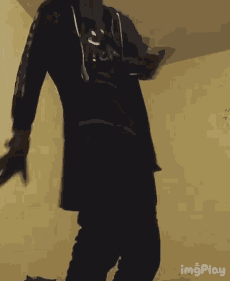 a man in a black shirt and black pants is standing in a room with his arms outstretched .