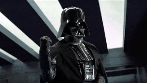 darth vader from star wars is wearing a helmet and making a fist .