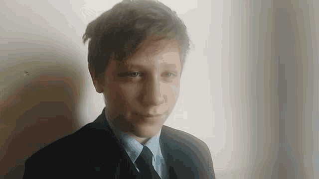 a young man wearing a suit and tie looks at the camera