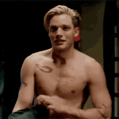 a shirtless man with a tattoo on his arm is standing in a dark room .