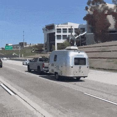 an airstream trailer is pulled by a truck on a highway with a green sign above it that says freeway