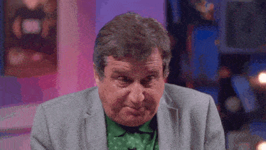 a man in a suit and green shirt makes a funny face
