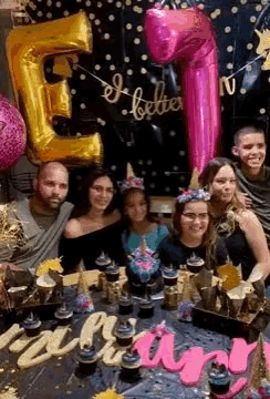 a group of people are posing for a picture at a birthday party with balloons and cupcakes