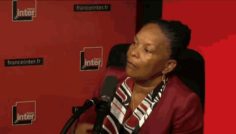 a woman speaking into a microphone in front of a red wall that says franceinter