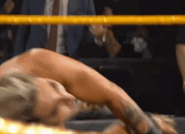 a woman is laying on the ground in a wrestling ring while a man in a suit watches .