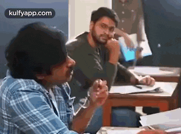 a group of men are sitting at a table in a classroom talking to each other .
