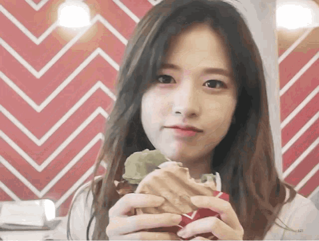 a girl eating a sandwich in front of a red and white chevron patterned wall