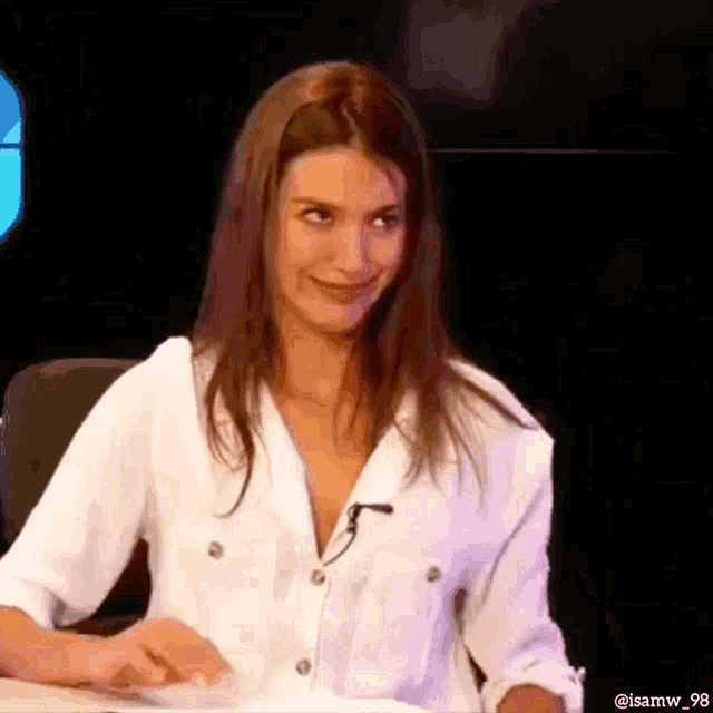 a woman in a white shirt is sitting at a table with a microphone .