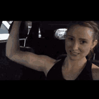 a woman is sitting in a car flexing her muscles .