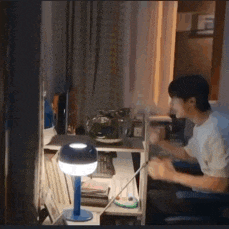 a man is sitting at a desk in front of a window with a lamp on it .
