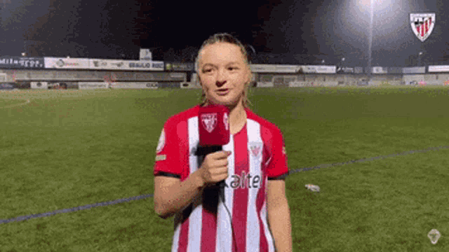 a woman in a striped shirt is holding a microphone on a soccer field