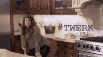 a woman is squatting on a counter in a kitchen with #twerk written on the wall