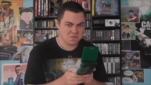 a man in a black shirt is holding a video game in front of a wall that has a poster that says ca bl
